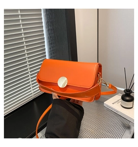 Detail of orange leather crossbody bag featuring a round metallic clasp and smooth texture