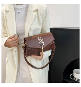 Detail of brown faux leather handbag with crocodile pattern, golden S logo and tassel