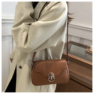 Dettaglio borsa a tracolla in pelle marrone con fibbia in metallo argento su un trench beige