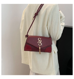Detail of burgundy crossbody bag with gold SS logo, tassel, and faux croc texture