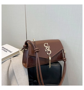 Detail of brown leather handbag featuring crocodile texture and metallic tassel logo