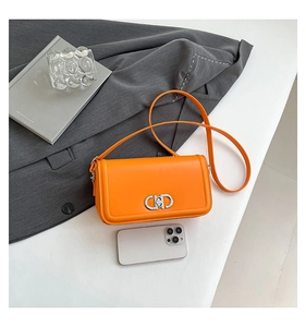 Close-up of bright orange crossbody bag with silver interlocking clasp and phone for scale
