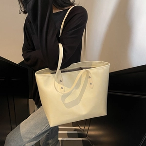 Large beige leather tote bag for women shown on shoulder in stylish urban setting