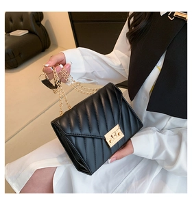 Detail of black quilted chain bag with V-shaped stitching and golden lock closure