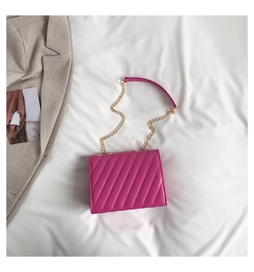 Detailed quilted texture of a bright pink chain crossbody bag on white fabric