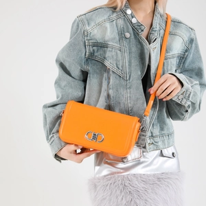 Chic orange faux leather crossbody bag with silver buckle on a denim jacket background