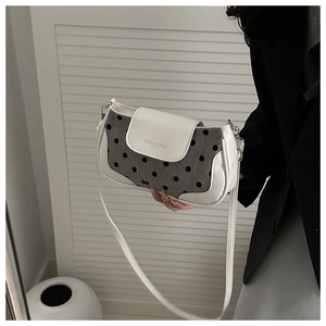 Detailed view of grey polka dot fabric and white leather trim on crossbody bag