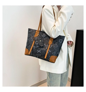 Detailed close-up of large letter-print tote bag with brown leather handles and matching pouch