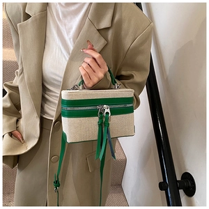 Detail of canvas box bag with green trim and long leather tassels on a model