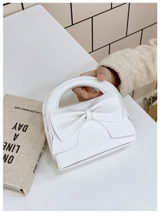 Close-up of a white mini handbag with a large bow and elegant lychee grain texture
