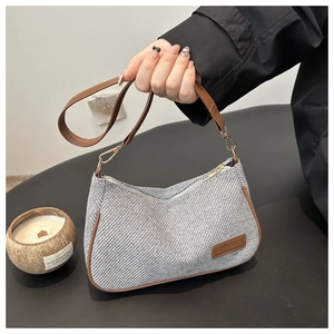 Close-up of grey herringbone fabric and brown leather trim on minimalist handbag