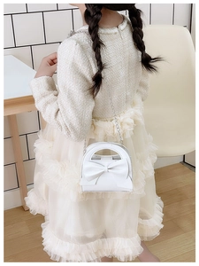 Girl wearing a white bow handbag with chain strap over a tweed top and mesh skirt
