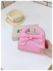 Detailed view of pink mini PU handbag with a large bow on a minimalist desktop
