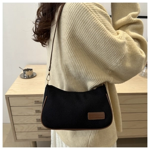 Detailed side view of black fabric shoulder bag with brown leather trim on beige knitwear