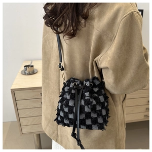 Detail of checkered denim bucket bag featuring frayed woven texture and leather drawstring