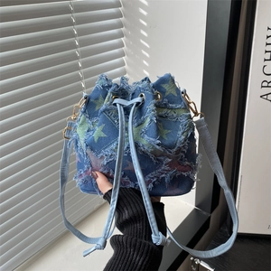 Detail of blue denim bucket bag with distressed star patches and leather drawstring closure