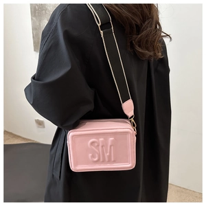 Pink crossbody bag with embossed SM logo and striped fabric strap on a model