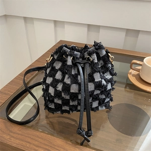 Detail of checkered denim bucket bag featuring fringe trim and black leather drawstring