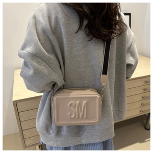 Side view of beige crossbody bag with embossed letters and wide woven shoulder strap