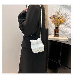 Close-up of white quilted mini bag with oversized bow design and gold metal chain strap