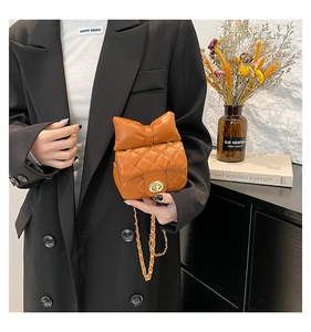 Close-up of caramel quilted leather bag with large bow and golden metal chain strap