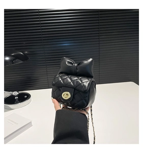 Close-up of black quilted mini bag with oversized leather bow and gold chain strap