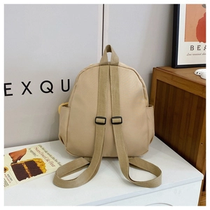 Detail view of adjustable fabric straps and side pockets on a beige canvas backpack