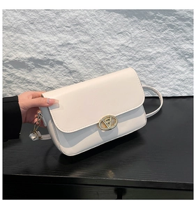 Détail du sac bandoulière en cuir PU blanc avec boucle dorée en V sur surface sombre