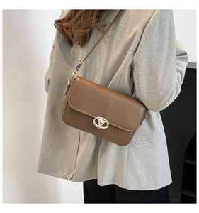 Détail d'un sac porté épaule en cuir marron avec fermoir doré sur une veste grise