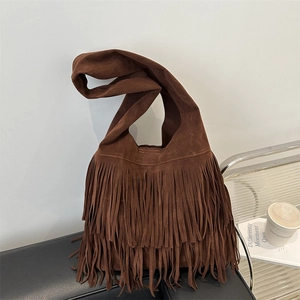 Donkerbruine suède tote bag met bohemian franjes op een stijlvolle leren bank