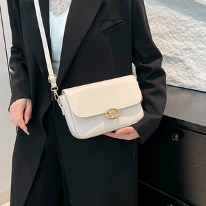 Sac bandoulière beige minimaliste avec boucle dorée porté par un mannequin de profil