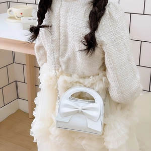 White girls cross-body bag with large bow and silver chain strap shown with a model