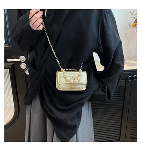 Detail of gold croc-effect mini bag with pearl handle and metal chain on a model