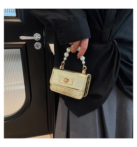 Detailed shot of golden crocodile-embossed mini handbag with elegant pearl handle and metal lock