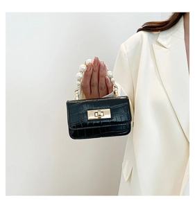 Detail of a black croc-embossed mini bag featuring a large pearl handle and gold twist lock