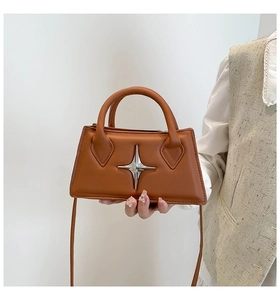 Gros plan du sac trapèze beige avec emblème en métal étoilé et poignée supérieure