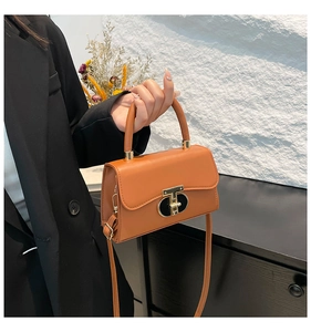 Detail of caramel leather handbag featuring a distinct golden T-shaped metal twist lock