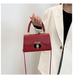 Detailed view of red leather handbag featuring a gold double-T metal clasp and handle