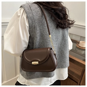 Detail of dark brown leather underarm bag featuring a golden cylindrical clasp
