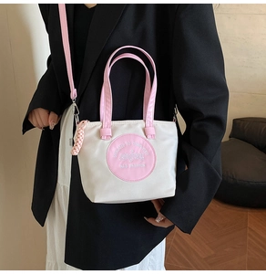Gros plan du sac cabas contrasté rose et blanc avec broderie et détail de pendentif