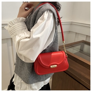 Detail of red shoulder bag featuring a wave-edge flap and golden textured metal twist lock