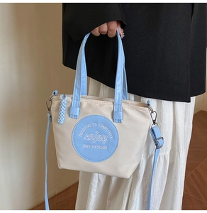Détail du sac cabas en toile avec lanières en cuir bleu et écusson brodé circulaire