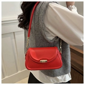Detail of a bright red crossbody bag featuring a golden cylindrical rotating lock and chain strap