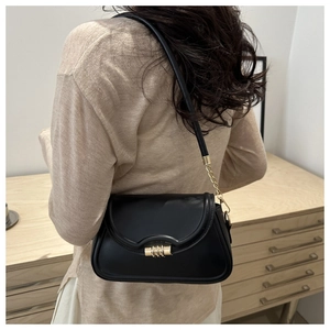 Detail of a black leather shoulder bag with gold twist lock worn by a model in a room