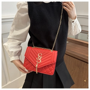 Detail of red quilted shoulder bag with gold SS logo, tassel and chain strap on model