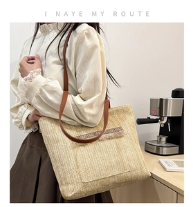 Detalle de bolso tote de paja bohemio con correas de cuero marrón y bolsillo con borla