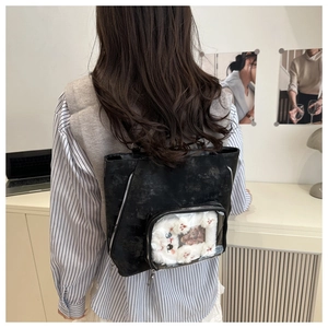 Detail view of a black ita bag with transparent window showing white plush kitten accessory
