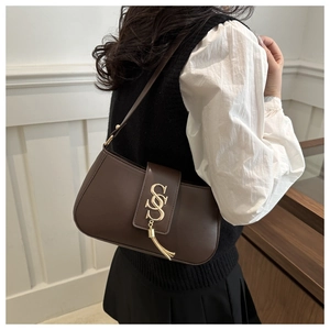 Model wearing dark brown leather shoulder bag with gold letter clasp and fringe detail