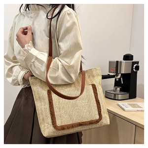 Detalle del bolso tote de paja con correas de cuero marrón y detalles de bolsillo con flecos