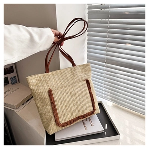 Detalle del bolso tote de paja trenzada con asas de cuero marrón y bolsillo de flecos